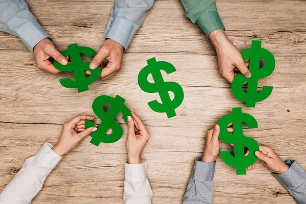 Top view of businesspeople holding dollar signs at wooden table, cropped view — Stock Photo
