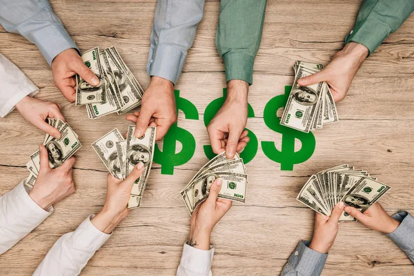 Top view of business partners holding dollar banknotes with dollar signs on table, cropped view — Stock Photo
