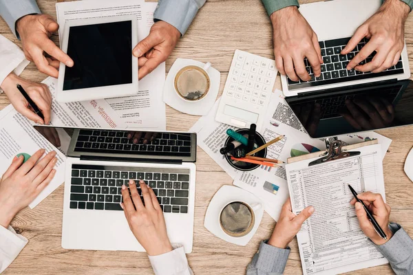 Vista superior de los socios comerciales con papeleo, gadgets y café en la mesa, vista recortada - foto de stock