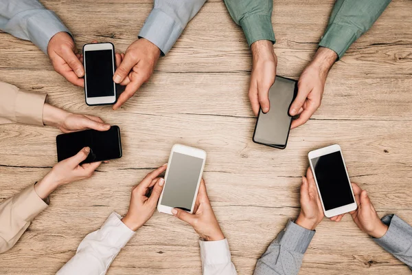 Top view of business people holding smartphones with blank screens on table, cropped view — Stock Photo