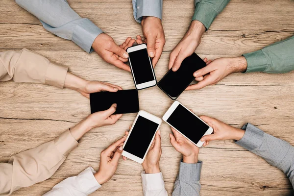 Top view of business people holding smartphones at wooden table, cropped view — Stock Photo