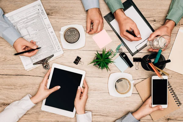 Vista dall'alto dei colleghi che lavorano con gadget e documenti con caffè sul tavolo, vista ritagliata — Foto stock