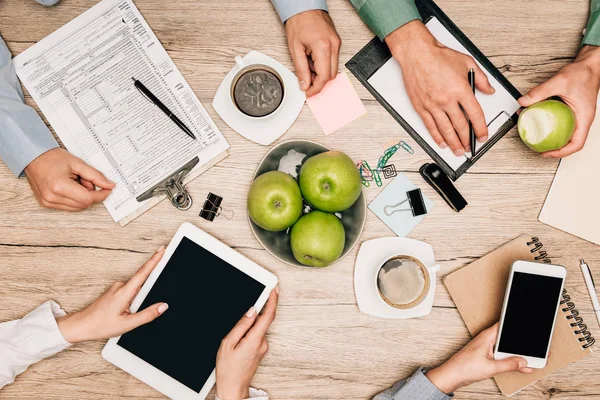 Vista superior de los colegas que trabajan con documentos, teléfonos inteligentes y tabletas digitales en la mesa de madera - foto de stock