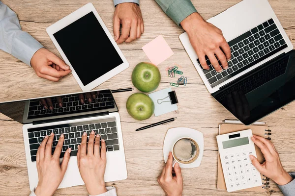 Vista superior de cuatro personas de negocios que utilizan computadoras portátiles, tableta digital y calculadora en la mesa - foto de stock