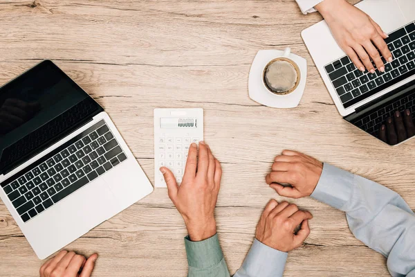 Top view of business people using laptops and calculator by coffee on table, cropped view — Stock Photo