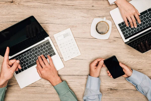 Vista dall'alto degli uomini d'affari che lavorano con laptop e smartphone con calcolatrice e caffè sul tavolo — Foto stock