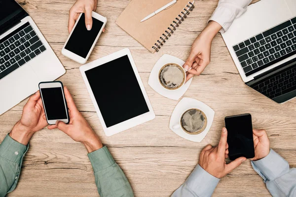 Ansicht von Geschäftspartnern mit Gadgets neben Kaffee auf dem Tisch, beschnittene Ansicht — Stockfoto