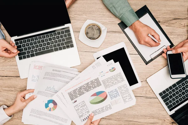 Top view of businesspeople with digital devices, documents and coffee on table, cropped view — Stock Photo