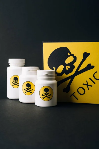 Jars and card with toxic sign isolated on black — Stock Photo