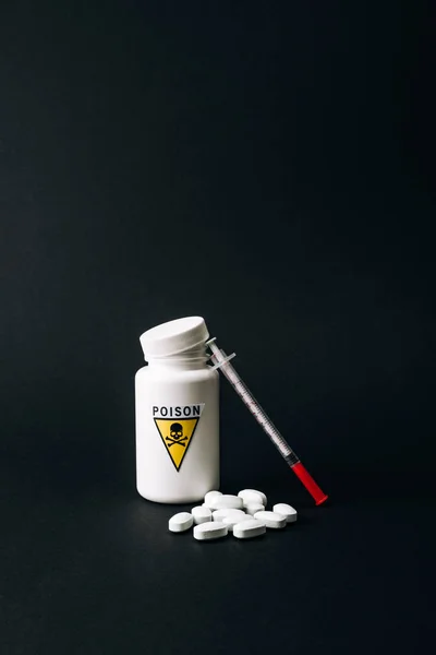 Jar with poison sign with pills and syringe isolated on black — Stock Photo