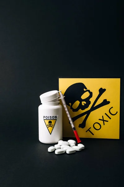 Jar with poison signs by pills and syringe isolated on black — Stock Photo