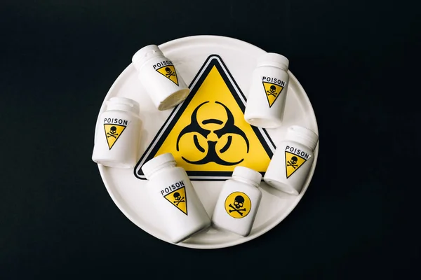 Top view of bottles with poison sign on plate with biohazard symbol isolated on black — Stock Photo