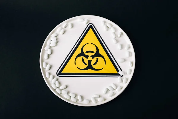 Top view of plate with pills and biohazard symbol isolated on black — Stock Photo