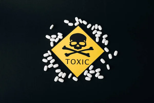 Top view of pills and toxic sign isolated on black — Stock Photo