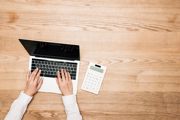 Ansicht von oben: Geschäftsfrau benutzt Laptop mit Taschenrechner auf Holztisch, beschnittene Ansicht — Stockfoto