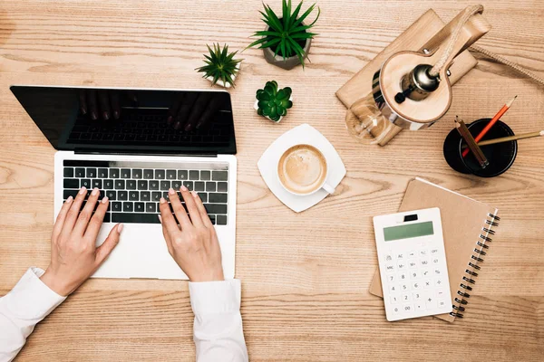 Top view of businesswoman using laptop by coffee and calculator on table, cropped view — Stock Photo