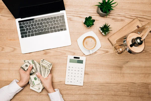 Вид сверху на предпринимательницу, держащую долларовые банкноты с ноутбуком и калькулятором на столе — стоковое фото