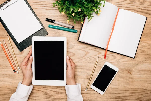 Ansicht von oben: Geschäftsfrau hält digitales Tablet mit Smartphone und Schreibwaren auf Tisch, beschnittene Ansicht — Stockfoto