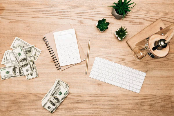 Vue du dessus des billets en dollars avec calculatrice et clavier d'ordinateur sur table en bois — Photo de stock