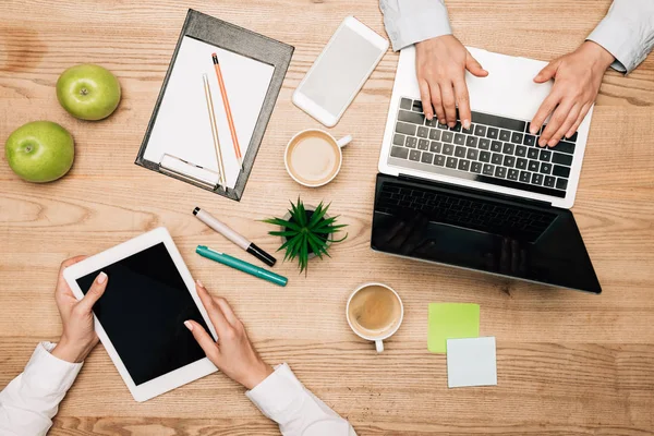 Top view of colleagues using digital tablet and laptop by coffee and stationery on table — Stock Photo