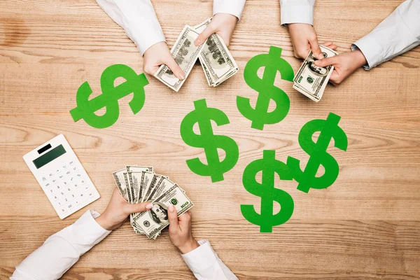 Top view of business partners holding cash beside calculator and dollar signs on table — Stock Photo