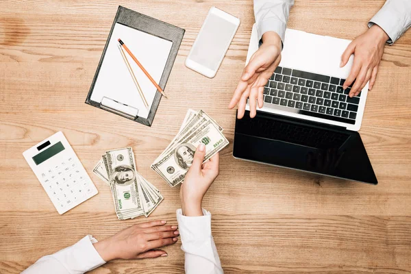 Vue d'ensemble des partenaires commerciaux avec billets en dollars, ordinateur portable et calculatrice sur table — Photo de stock