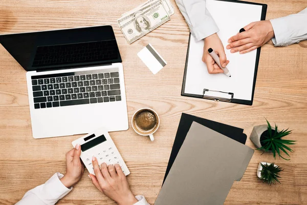 Вид сверху на бизнес-партнеров, работающих с калькулятором, деньги и ноутбук на столе, обрезанный вид — стоковое фото