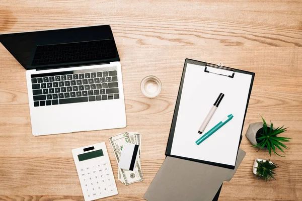 Top view of laptop, dollar banknotes with calculator and credit card on wooden table — Stock Photo