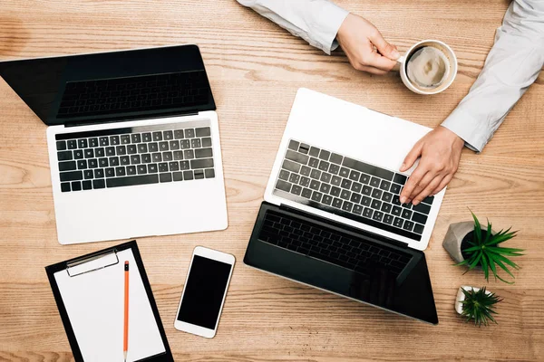 Vista superior do homem de negócios usando laptop enquanto bebe café na mesa, vista cortada — Fotografia de Stock