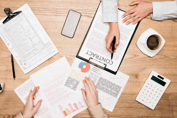 Top view of businesspeople working with contract and documents by calculator and coffee on table — Stock Photo