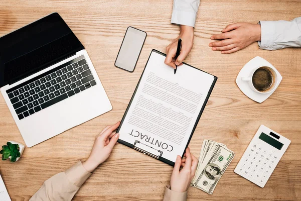 Vista superior de parceiros de negócios assinam contrato por laptop, notas de dólar e café na mesa, vista cortada — Fotografia de Stock