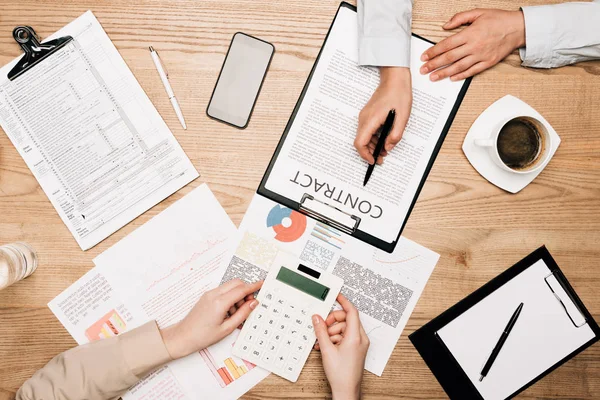 Top view of businesspeople colleagues with contract, calculator and paperwork on table, cropped view — Stock Photo