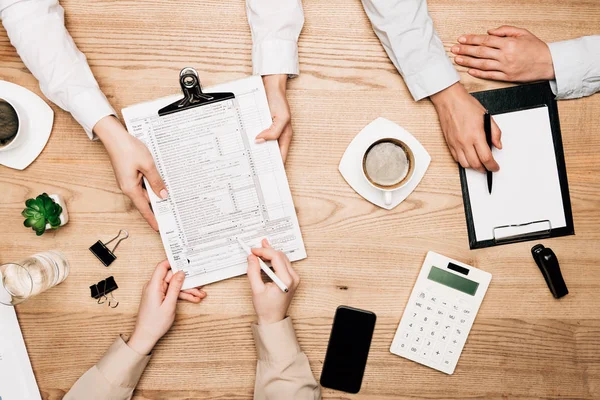 Draufsicht von Geschäftsleuten mit Papierkram, Taschenrechner und Kaffee auf dem Tisch, ausgeschnittene Ansicht — Stock Photo