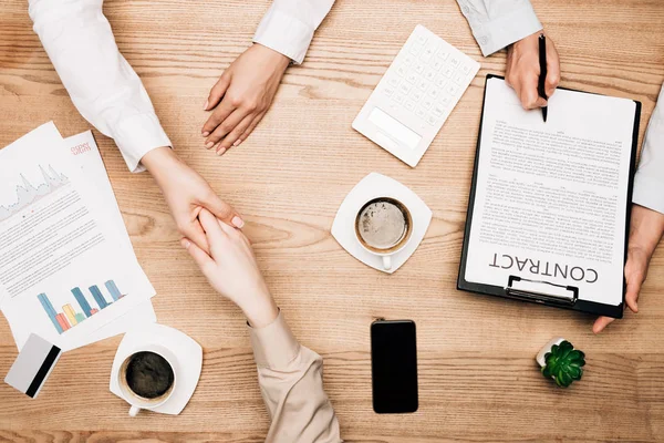 Vista superior dos parceiros de negócios apertando as mãos perto do contrato, café e cartão de crédito na mesa — Fotografia de Stock