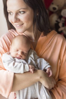 Güzel bir kadın kucağında yeni doğmuş bir bebeği tutuyor.