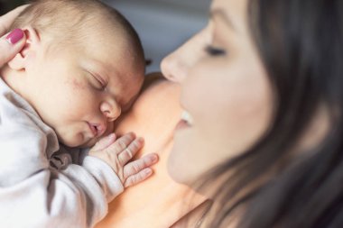 Güzel bir kadın kucağında yeni doğmuş bir bebeği tutuyor.