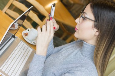 Genç işkadını iken açık dizüstü bilgisayar önünde oturma Smartphone kullanarak