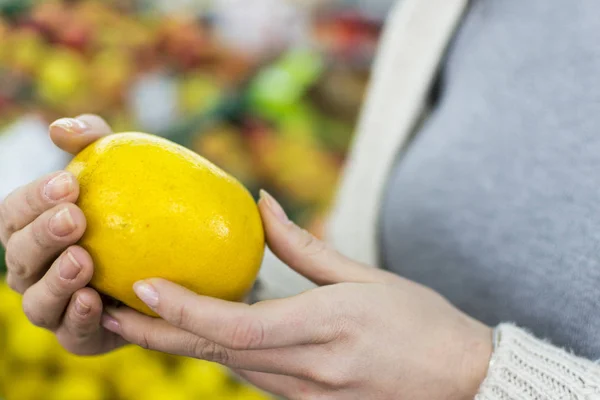 Woman holding a lemon in his hands in front of shelves with fruit -close up