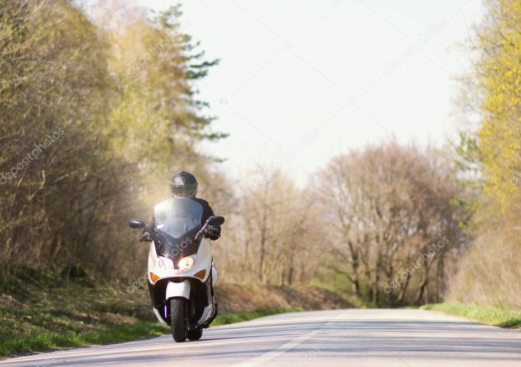 A man enjoys while riding a motorcycle scooter on roads out of town and crowds