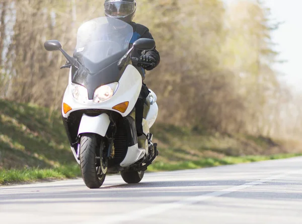 A mature man rides a motorcycle scooter on a journey out of town