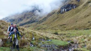 Azuay, Ekvador - 12 Aralık 2019: Cajas Ulusal Parkı 'nda dağlık alanda yürüyüş yapan turistler bulutlu bir günde Tres Cruses' u geçtiler.