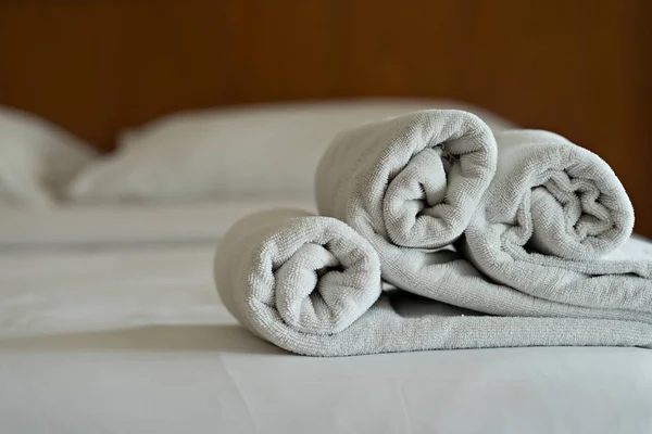 White towels roll on bed in hotel bedroom
