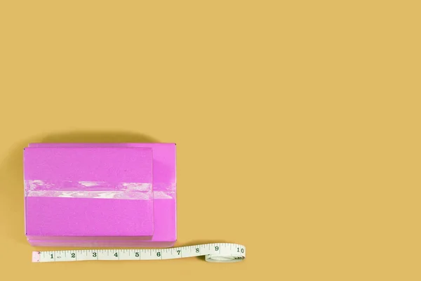 Top view pink box with tape measure on yellow background. — Stock Photo, Image