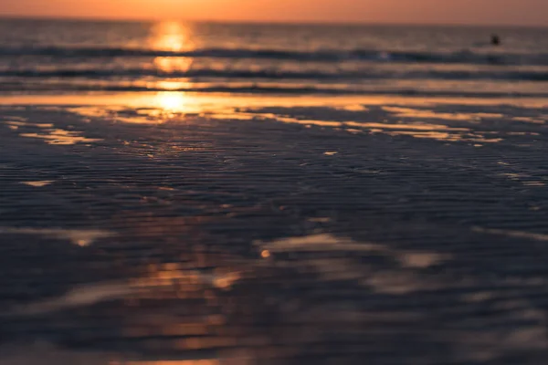 Belo pôr do sol com mar e praia. Pessoas desfocadas nadando — Fotografia de Stock