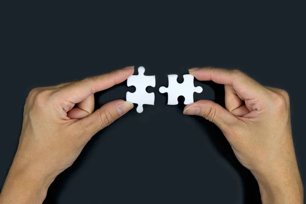 Siyah bir arka plan üzerinde beyaz jigsaw tutan el. 