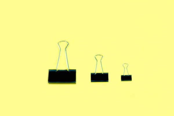 Três tamanhos para o grampo preto e metálico do ligante no amarelo — Fotografia de Stock