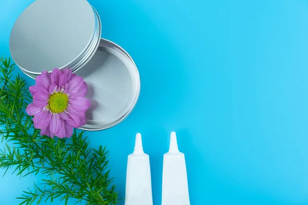 Kosmetiktuben und Blume mit Kopierraum auf blauem Hintergrund — Stockfoto