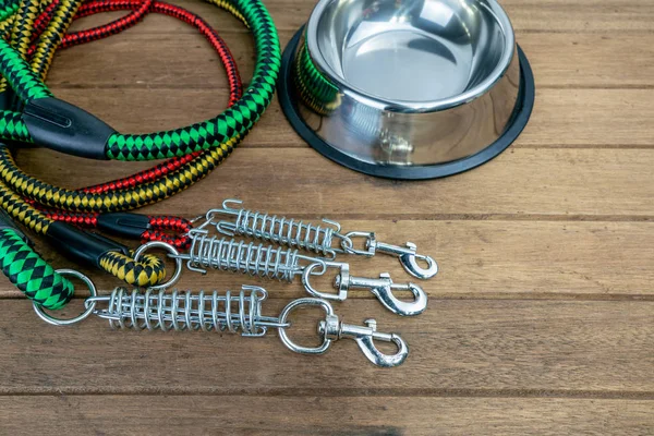 Pet leashes with hook and stainless bowl on wooden table.