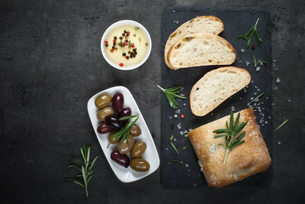 Italienska ciabatta bröd på svart skiffer med örter och Oliver. — Stockfoto