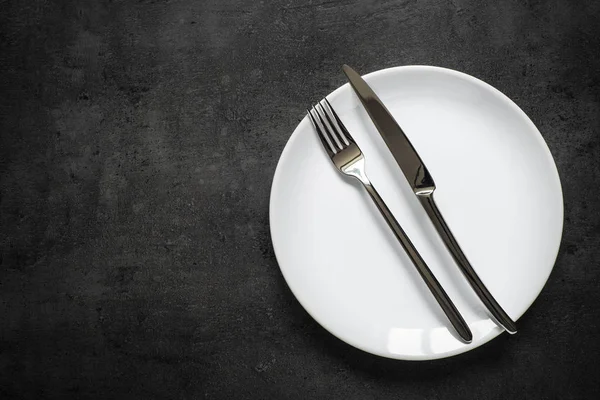 De instelling van de tabel. Vork-mes en witte plaat duikt met donkere leisteen tafel. — Stockfoto